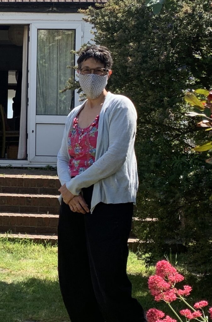 Katie wearing a fabric mask, standing in a garden