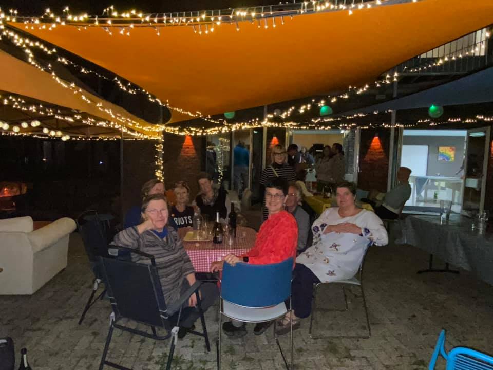 A group of people sitting at a table outdoors with an awning and lights. Katie is at the centre, in a red dress